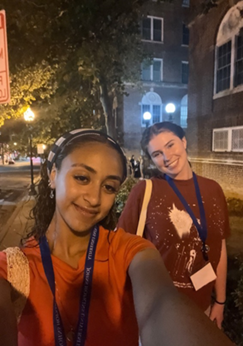 Two students pose for selfie at night outside with building in background