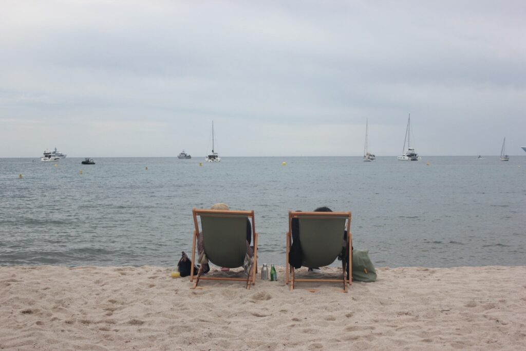 Two beach chairs facing the ocean with sailboats in the background