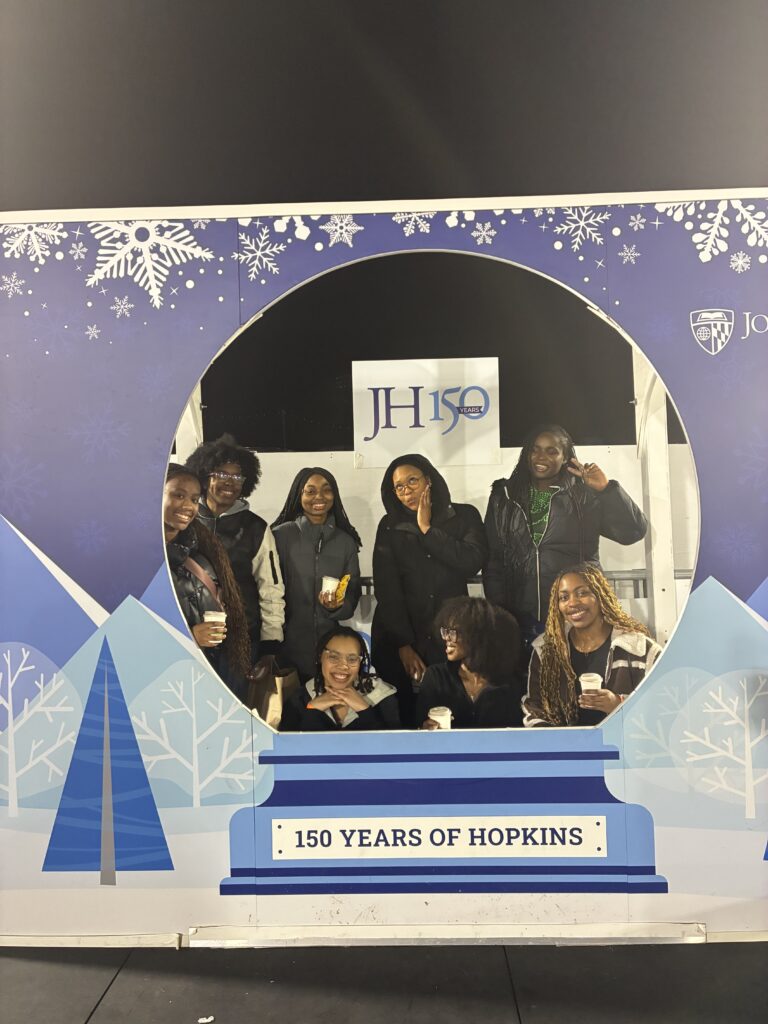 Members of Johns Hopkins' Black Women's Collective at the pop-up ice skating rink at Hopkins, posing in a snow globe cut out.